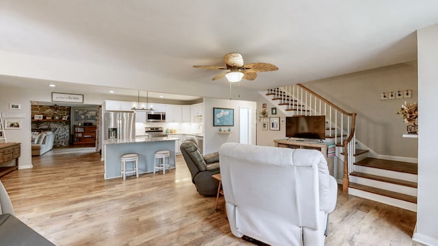 living room featuring a stone fireplace, ceiling fan with notable chandelier, and light hardwood / wood-style flooring