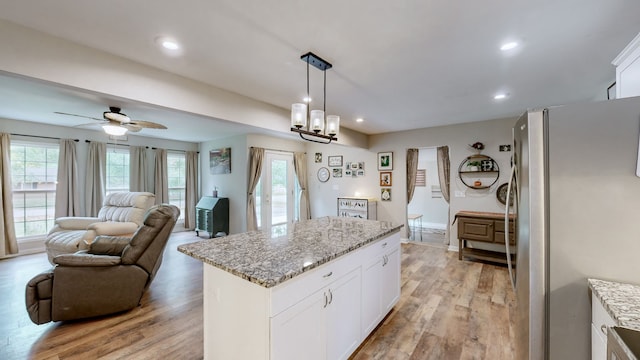 kitchen with pendant lighting, ceiling fan with notable chandelier, white cabinets, light hardwood / wood-style flooring, and stainless steel fridge