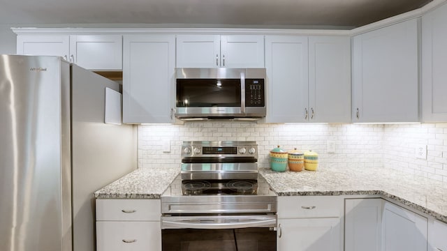 kitchen featuring light stone counters, white cabinets, stainless steel appliances, and decorative backsplash