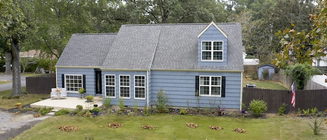 new england style home featuring a patio, a front lawn, and a shed