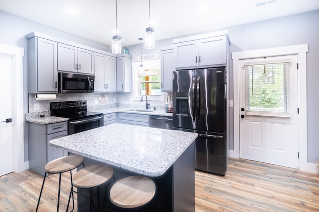 kitchen with pendant lighting, light wood-type flooring, sink, a kitchen island, and stainless steel appliances