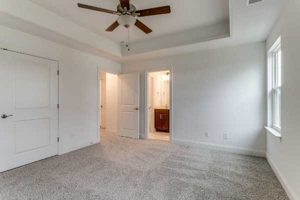 unfurnished bedroom featuring ensuite bathroom, light colored carpet, a tray ceiling, and ceiling fan