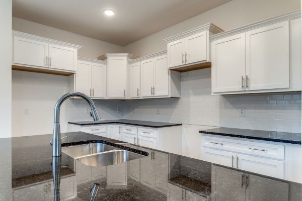 kitchen featuring white cabinets, dark stone countertops, sink, and backsplash