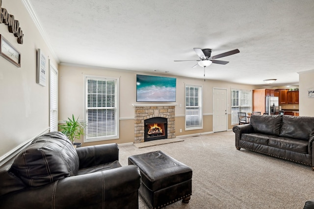 carpeted living room featuring ceiling fan, a stone fireplace, a textured ceiling, and crown molding