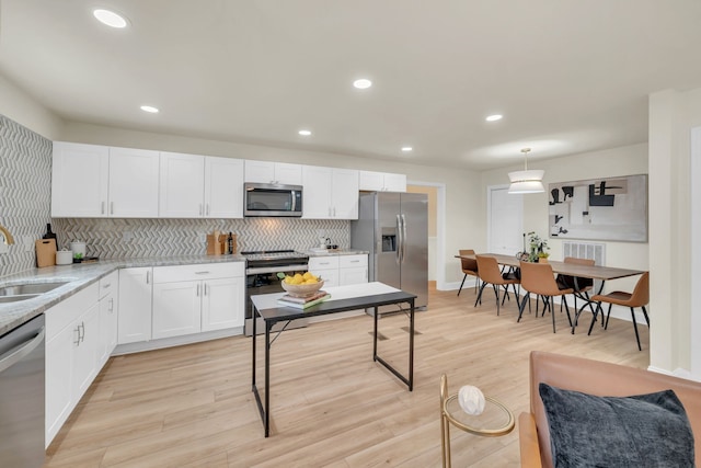 kitchen with decorative light fixtures, stainless steel appliances, light wood-type flooring, and white cabinets