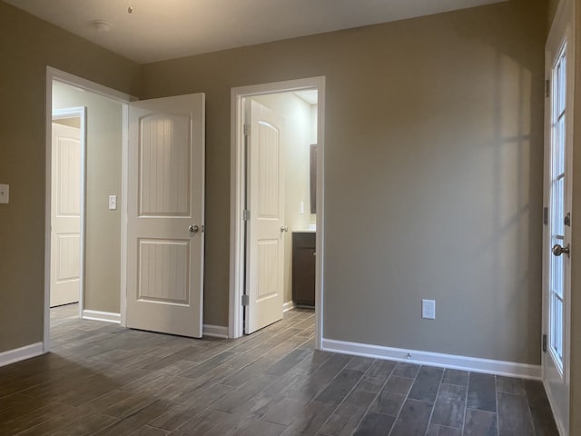 unfurnished bedroom featuring ensuite bathroom and dark hardwood / wood-style flooring