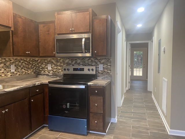 kitchen featuring appliances with stainless steel finishes, dark brown cabinetry, decorative backsplash, and light hardwood / wood-style flooring