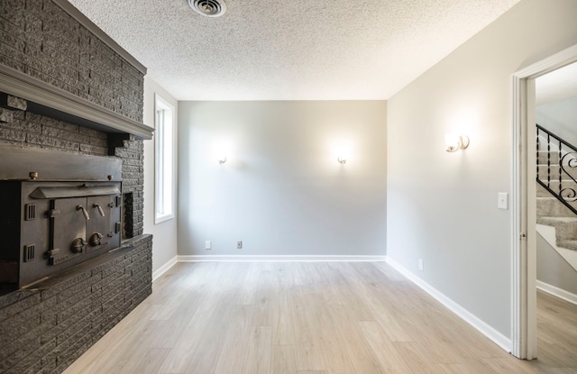 unfurnished living room with a brick fireplace, a textured ceiling, and light wood-type flooring