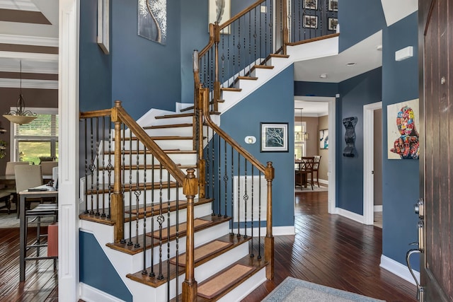 stairway with wood-type flooring, a towering ceiling, and ornamental molding