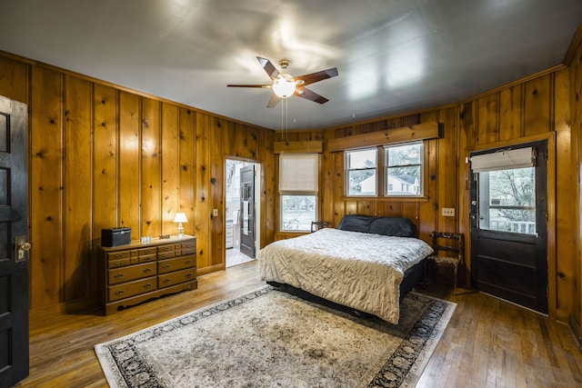 bedroom with ceiling fan, wood walls, crown molding, ensuite bathroom, and dark hardwood / wood-style flooring