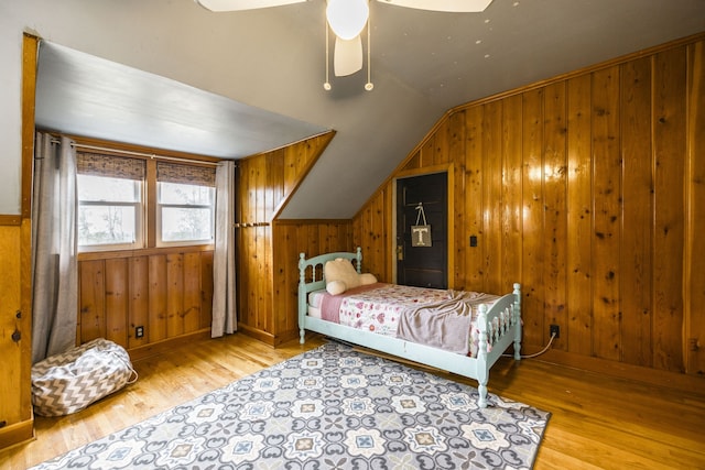 bedroom with light wood-type flooring, vaulted ceiling, ceiling fan, and wood walls