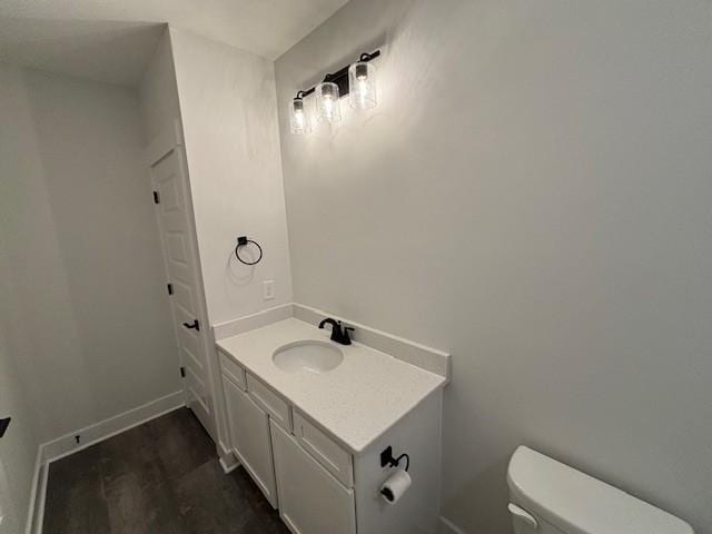 bathroom featuring toilet, vanity, wood finished floors, and baseboards
