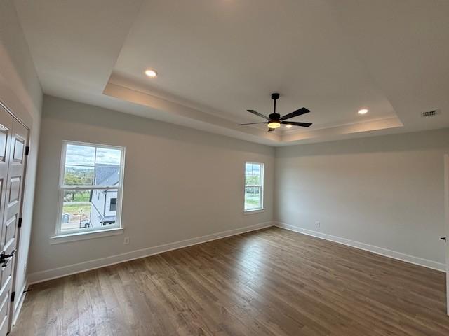 empty room with a raised ceiling, wood finished floors, and baseboards
