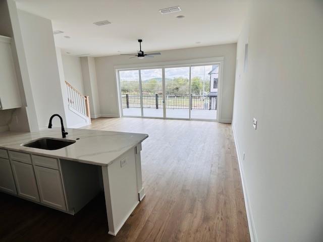 kitchen with a sink, open floor plan, a ceiling fan, wood finished floors, and light stone countertops