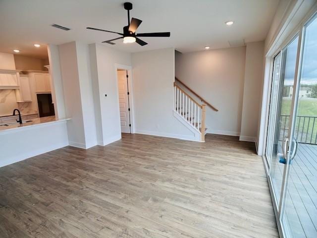 unfurnished living room featuring light wood-style floors, baseboards, visible vents, and stairs