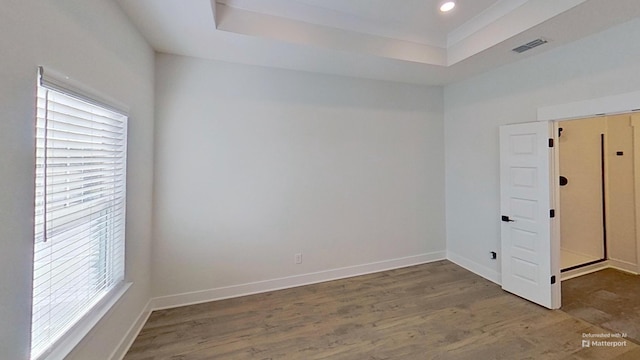 empty room with baseboards, wood finished floors, visible vents, and a raised ceiling