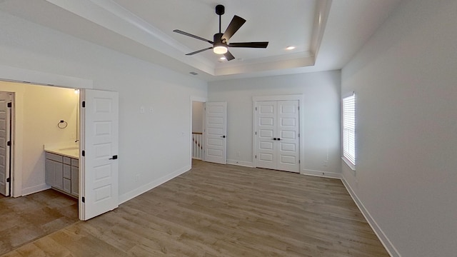 unfurnished bedroom with baseboards, a tray ceiling, and light wood-style floors