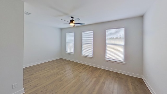 spare room with wood finished floors, a ceiling fan, visible vents, and a wealth of natural light