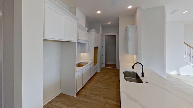 kitchen featuring light stone counters, a sink, light wood-style floors, white cabinets, and recessed lighting