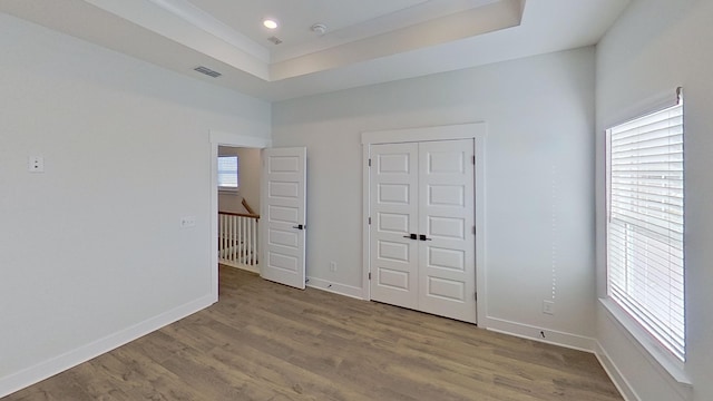 unfurnished bedroom featuring a raised ceiling, wood finished floors, and baseboards