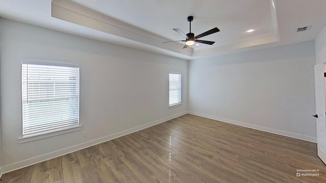 empty room with baseboards, recessed lighting, wood finished floors, ceiling fan, and a raised ceiling