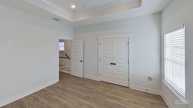 unfurnished bedroom featuring a raised ceiling, wood finished floors, and baseboards