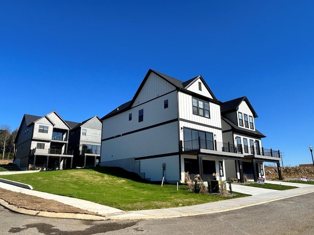 exterior space with board and batten siding, a balcony, and a front yard