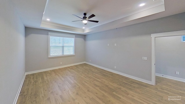 unfurnished room with baseboards, light wood-style floors, a ceiling fan, and a raised ceiling