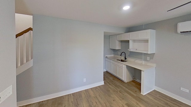 kitchen with light countertops, a sink, baseboards, light wood-style floors, and an AC wall unit