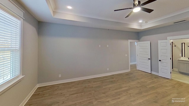 unfurnished bedroom with visible vents, baseboards, connected bathroom, a raised ceiling, and light wood-style floors