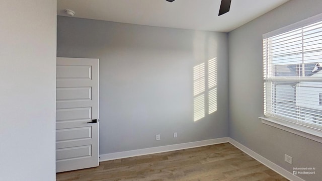 empty room with a wealth of natural light, wood finished floors, ceiling fan, and baseboards