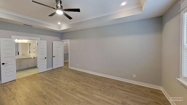 unfurnished bedroom featuring ensuite bathroom, visible vents, light wood-style flooring, baseboards, and a raised ceiling