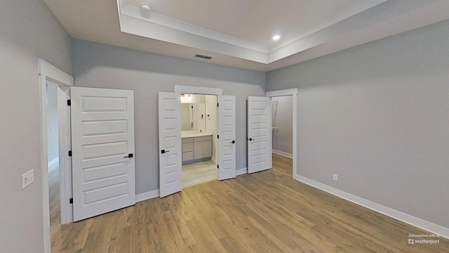 unfurnished bedroom featuring baseboards, a tray ceiling, visible vents, and light wood-type flooring