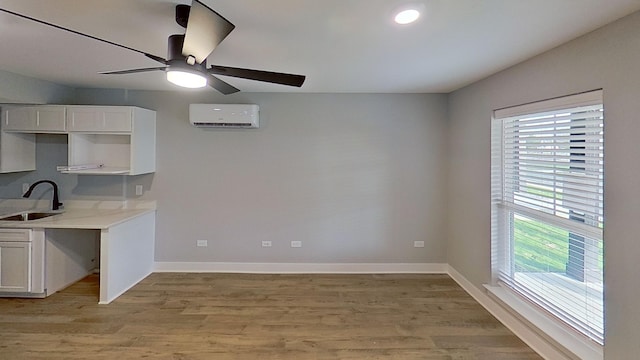 kitchen featuring light countertops, light wood-type flooring, a sink, ceiling fan, and a wall mounted air conditioner