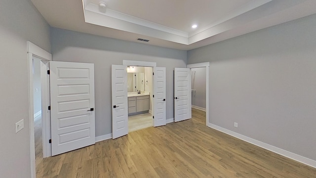 unfurnished bedroom featuring a tray ceiling, light wood-type flooring, baseboards, visible vents, and ensuite bathroom
