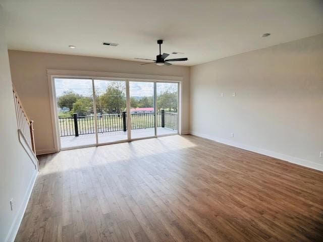 unfurnished living room featuring a ceiling fan, wood finished floors, baseboards, and stairs
