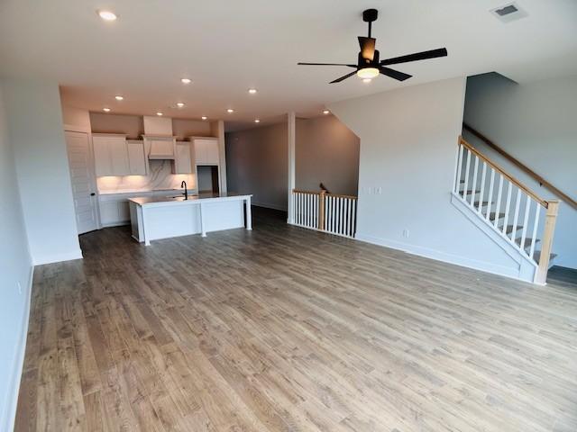 unfurnished living room featuring ceiling fan, light wood finished floors, recessed lighting, a sink, and baseboards