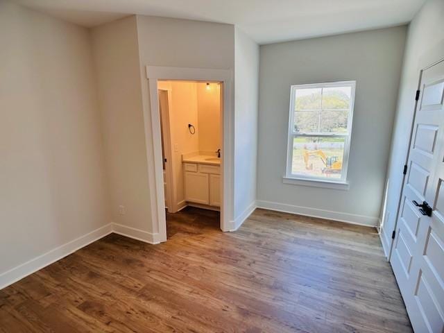 unfurnished bedroom with wood finished floors, baseboards, and a sink