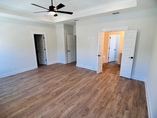 unfurnished bedroom featuring a raised ceiling, wood finished floors, baseboards, and ceiling fan