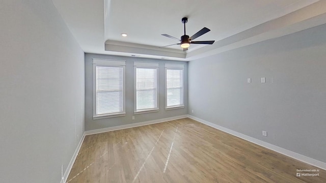 unfurnished room with a raised ceiling, baseboards, light wood-style flooring, and ceiling fan