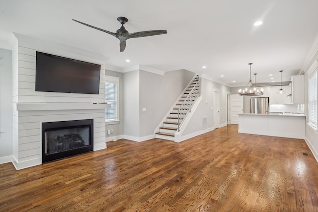 unfurnished living room with wood-type flooring, ceiling fan with notable chandelier, crown molding, and a large fireplace