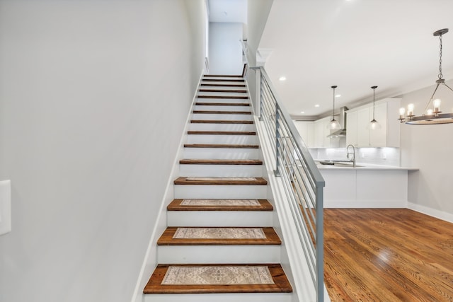 stairs featuring an inviting chandelier, hardwood / wood-style flooring, and sink