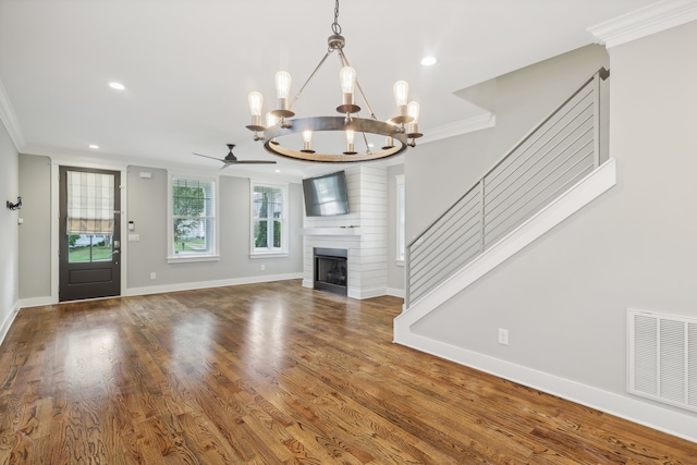 unfurnished living room featuring ceiling fan with notable chandelier, hardwood / wood-style floors, a fireplace, and crown molding