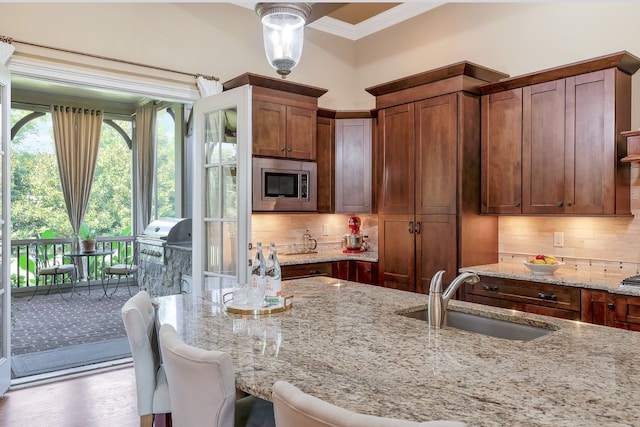 kitchen with light wood-type flooring, backsplash, stainless steel microwave, and sink