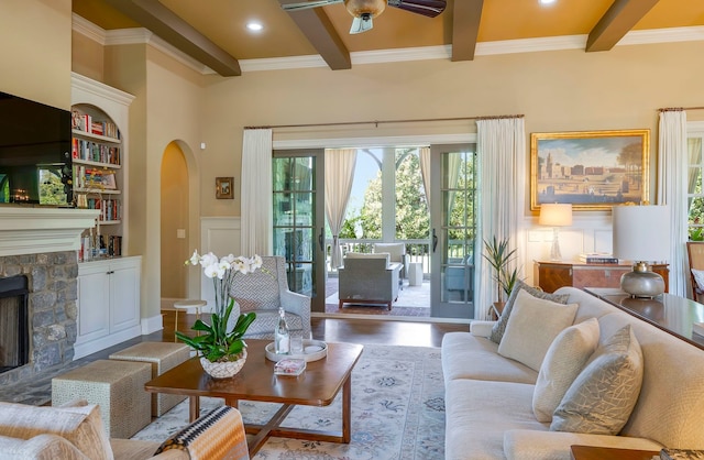 living room featuring beam ceiling, a fireplace, hardwood / wood-style floors, crown molding, and ceiling fan