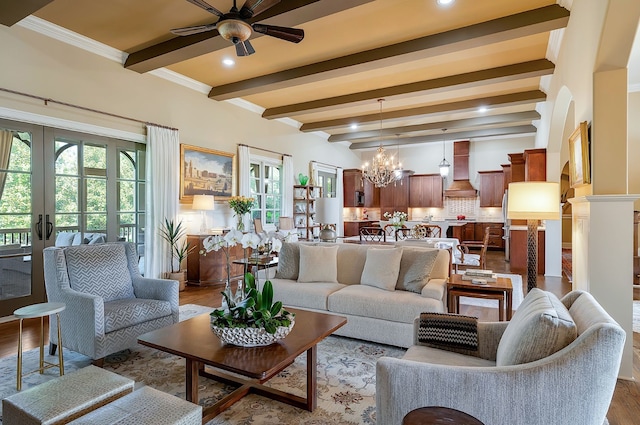 living room with ceiling fan with notable chandelier, beamed ceiling, wood-type flooring, french doors, and ornamental molding