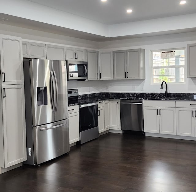 kitchen with dark stone counters, appliances with stainless steel finishes, dark hardwood / wood-style floors, and sink