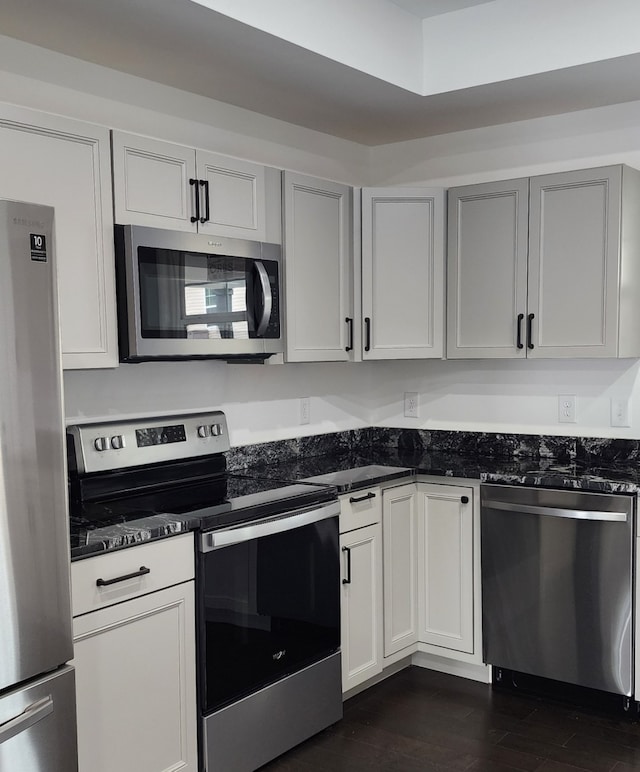 kitchen with gray cabinets, dark stone countertops, appliances with stainless steel finishes, and dark hardwood / wood-style flooring