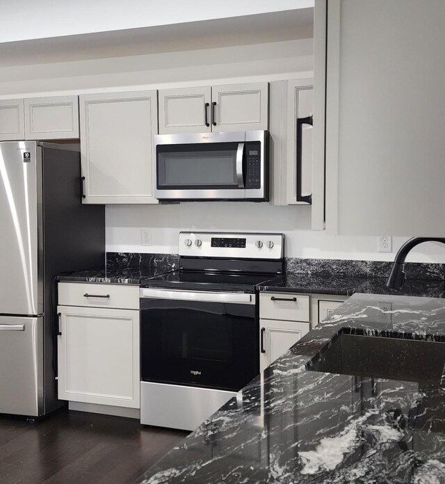 kitchen with dark stone countertops, dark wood-type flooring, stainless steel appliances, and white cabinets