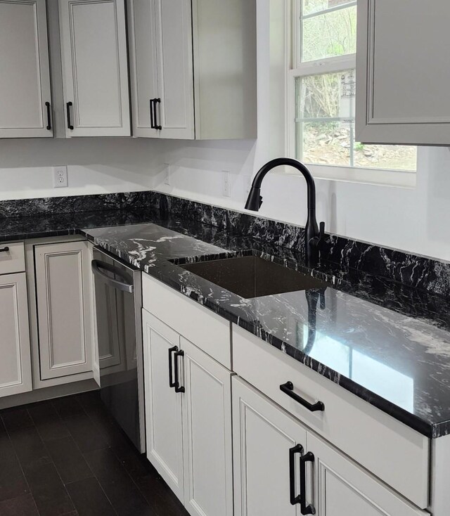 kitchen with dark stone counters, white cabinetry, dishwasher, and sink